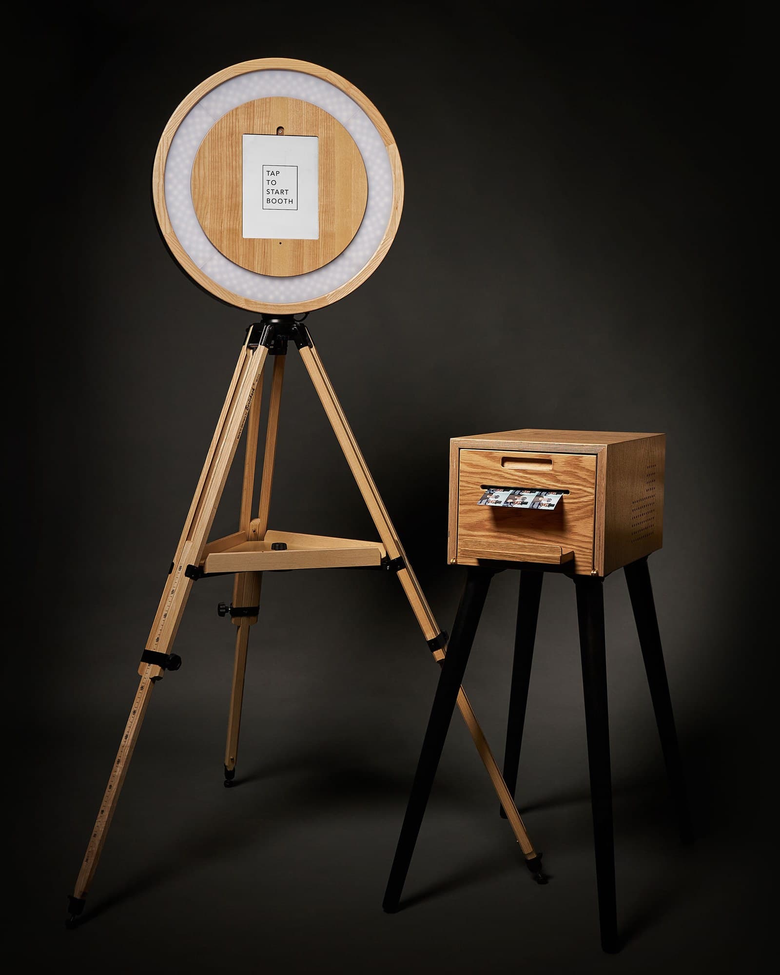Die Ringbooth mit ihrer Druckerbox im Studio: Holzring mit Ringlicht und Tablet auf einem Stativ, daneben der Drucker mit einem Fotostreifen