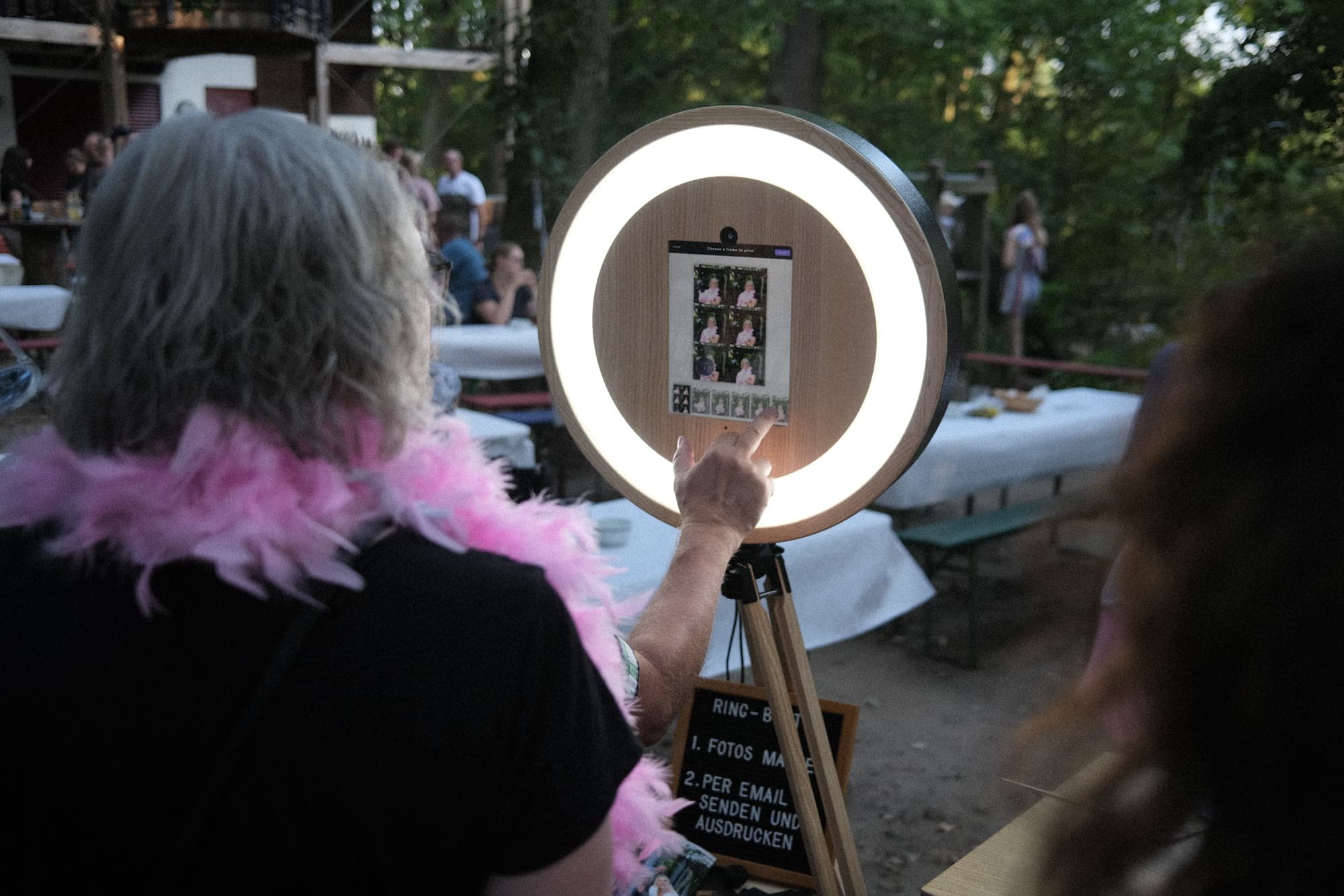 Ein Gast mit Federboa bedient die Fotobox bei einer Gartenfeier
